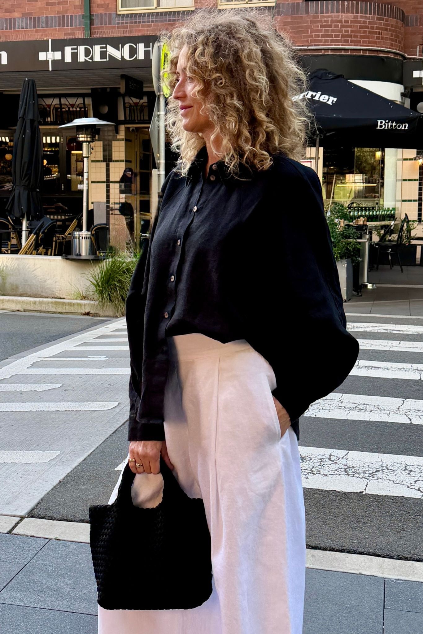 Woman wearing the Eira black linen shirt with white linen tailored trousers